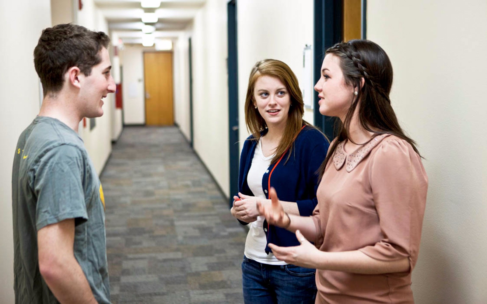 Three students standing and talking in a hallway dorm.