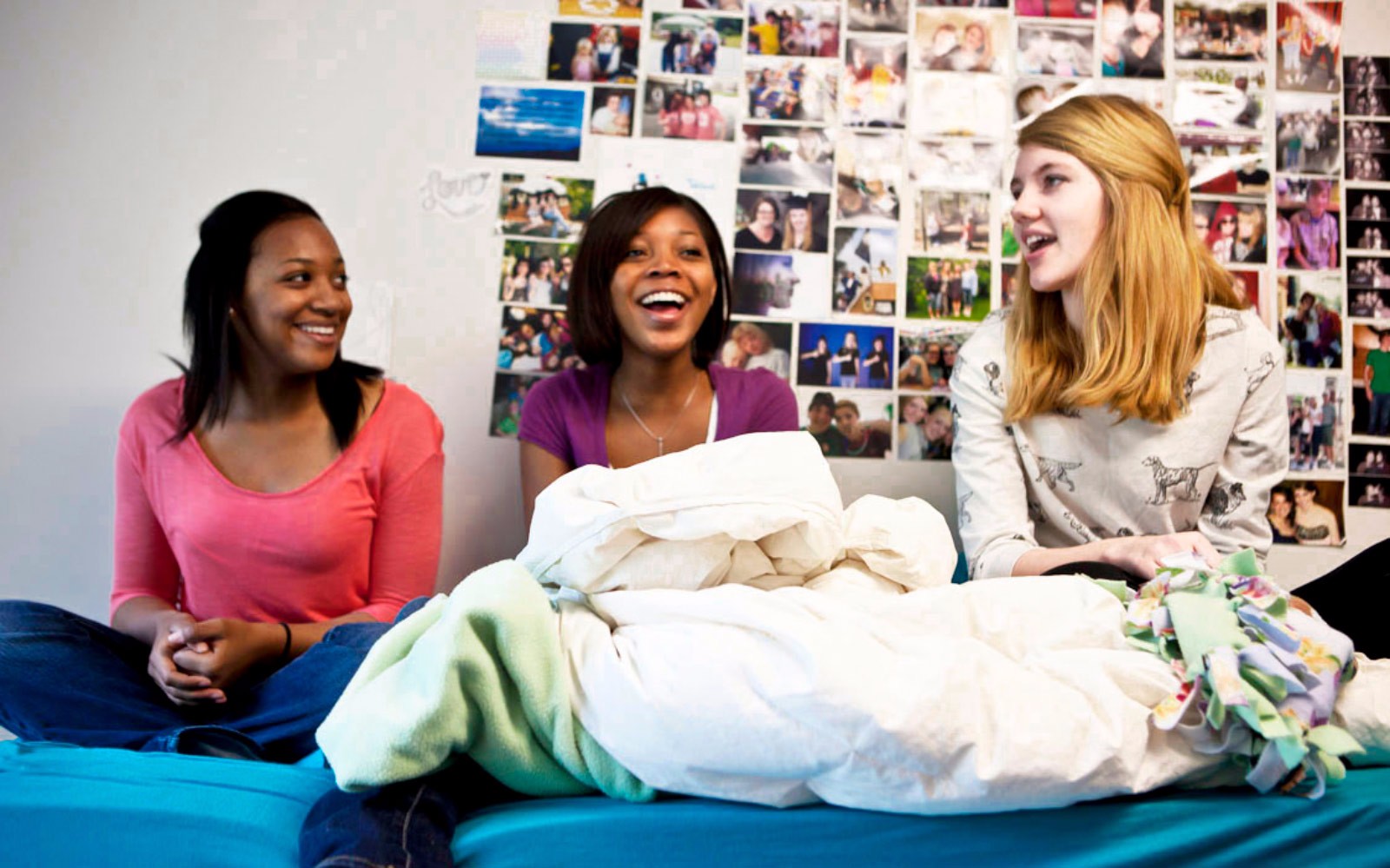 Three students sitting on a bed in a dorm room.