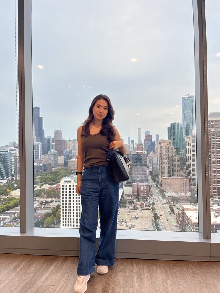 A young woman stands in front of a window overlooking the city