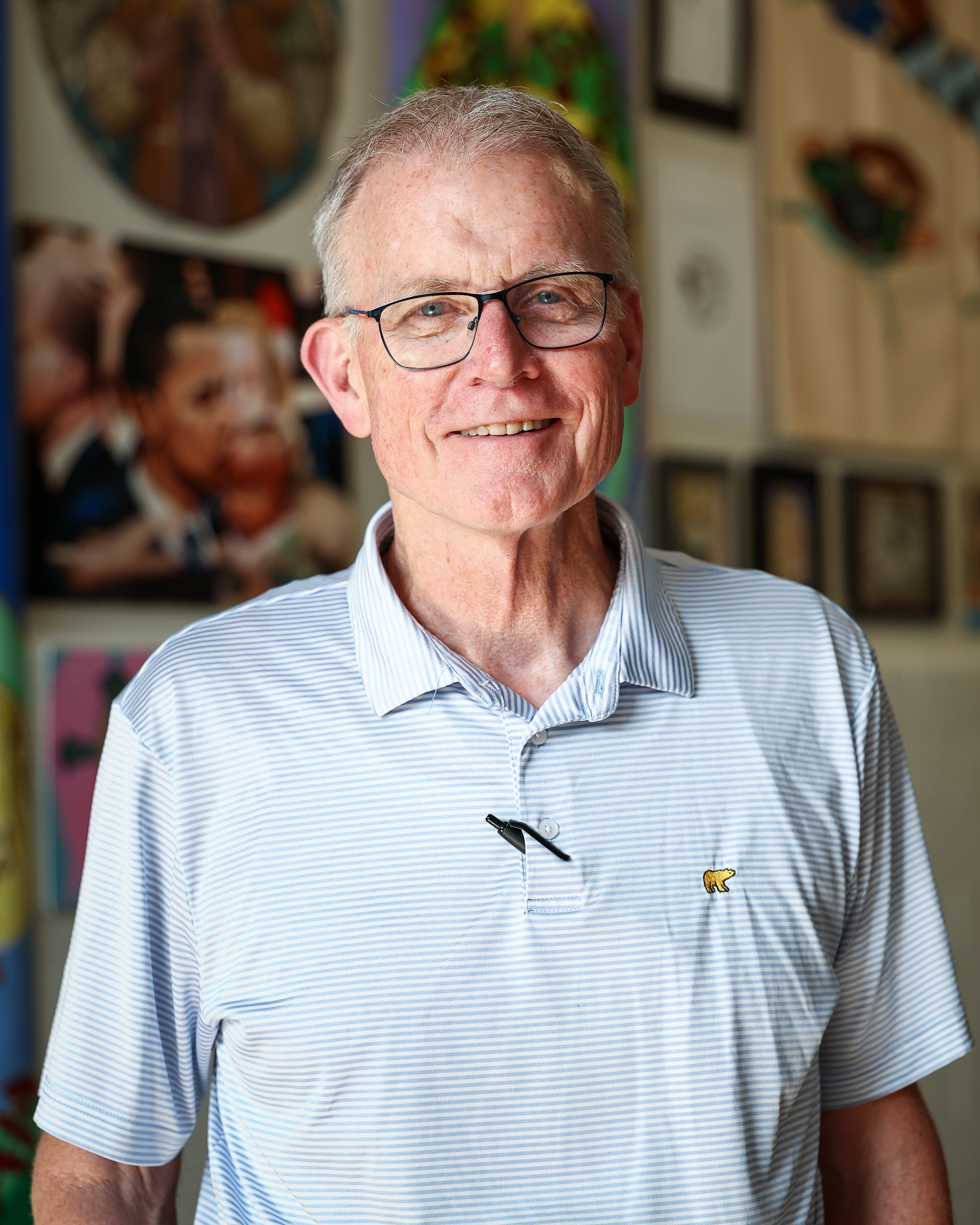 A man with white hair and glasses stands for a portrait